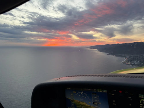 View from the cockpit of a training aircraft over Santa Monica Bay at sunset, the glare shield and panel in the foreground.
