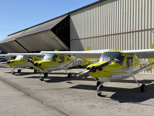 Three single-engine training aircraft parked nose-out in front of an open hangar.
